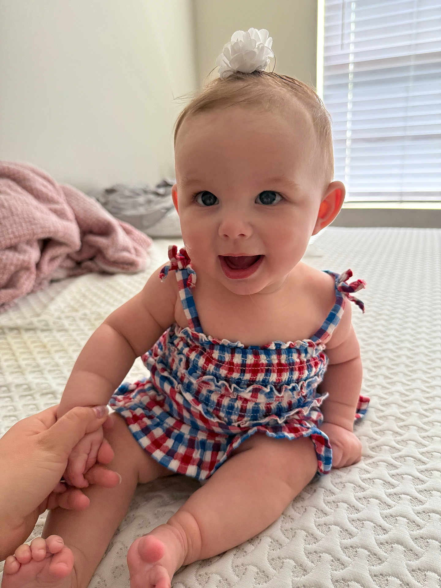 Aliviah is registered to the contest to win money with this photo: baby, child, smiling, sitting, dress, headband, flower, hand_holding, indoor, bed, blanket, window, light, happy, cute, skin, face, foot, person, infant