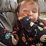 toddler, child, sleepy, onesie, patterned_clothing, couch, blanket, indoor, face, hand, hair, person, comfort, cozy, resting, casual, home, young_child, expression, relaxation