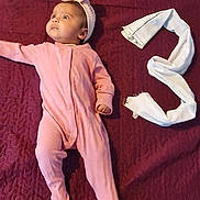 Duwaraka is registered to the contest to win money with this photo: baby, pink_onesie, headband, maroon_blanket, white_cloth, number_three, infant, lying_down, cute, portrait, child, soft_texture, indoors, looking_away, small_hand, footed_pajamas, blanket, fabric, resting, young_child