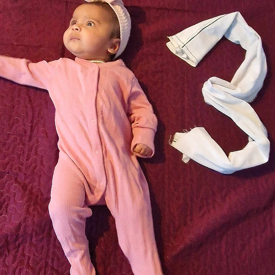 Duwaraka is registered to the contest to win money with this photo: baby, blanket, child, cute, fabric, footed_pajamas, headband, indoors, infant, looking_away, lying_down, maroon_blanket, number_three, pink_onesie, portrait, resting, small_hand, soft_texture, white_cloth, young_child