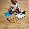 Antonio joined the competition — help win amazing prizes! toddler, child, baby, sitting, smiling, tongue_out, portrait, indoors, living_room, wooden_floor, pajamas, patterned_clothing, socks, bottle, cardboard, boxes, packaging, television, game_console, cables
