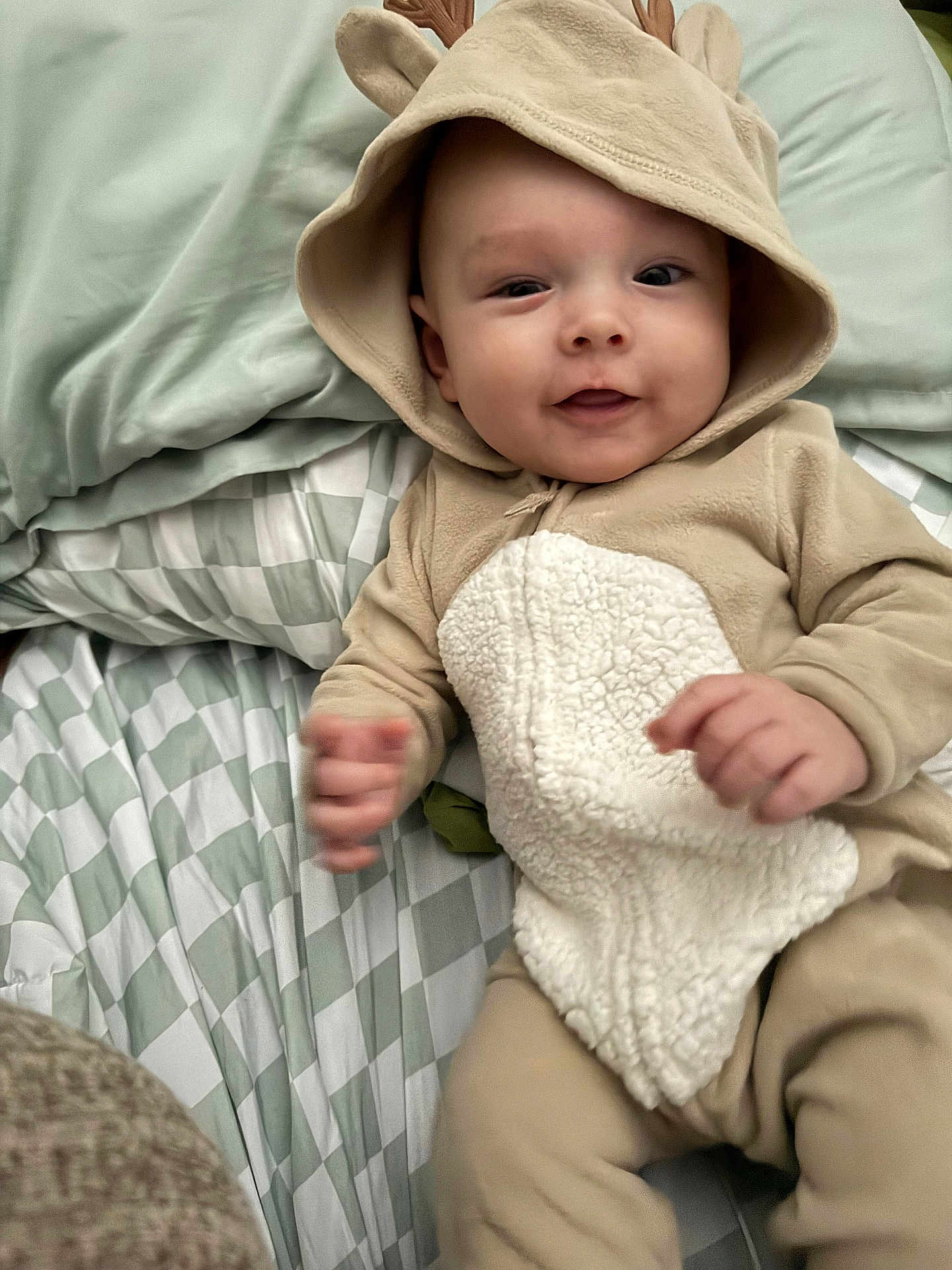 Myles joined the competition — help win amazing prizes! baby, infant, child, onesie, hood, antlers, bed, blanket, pattern, smile, cute, soft, hands, lying_down, cozy, indoor, sleepwear, young, person, portrait