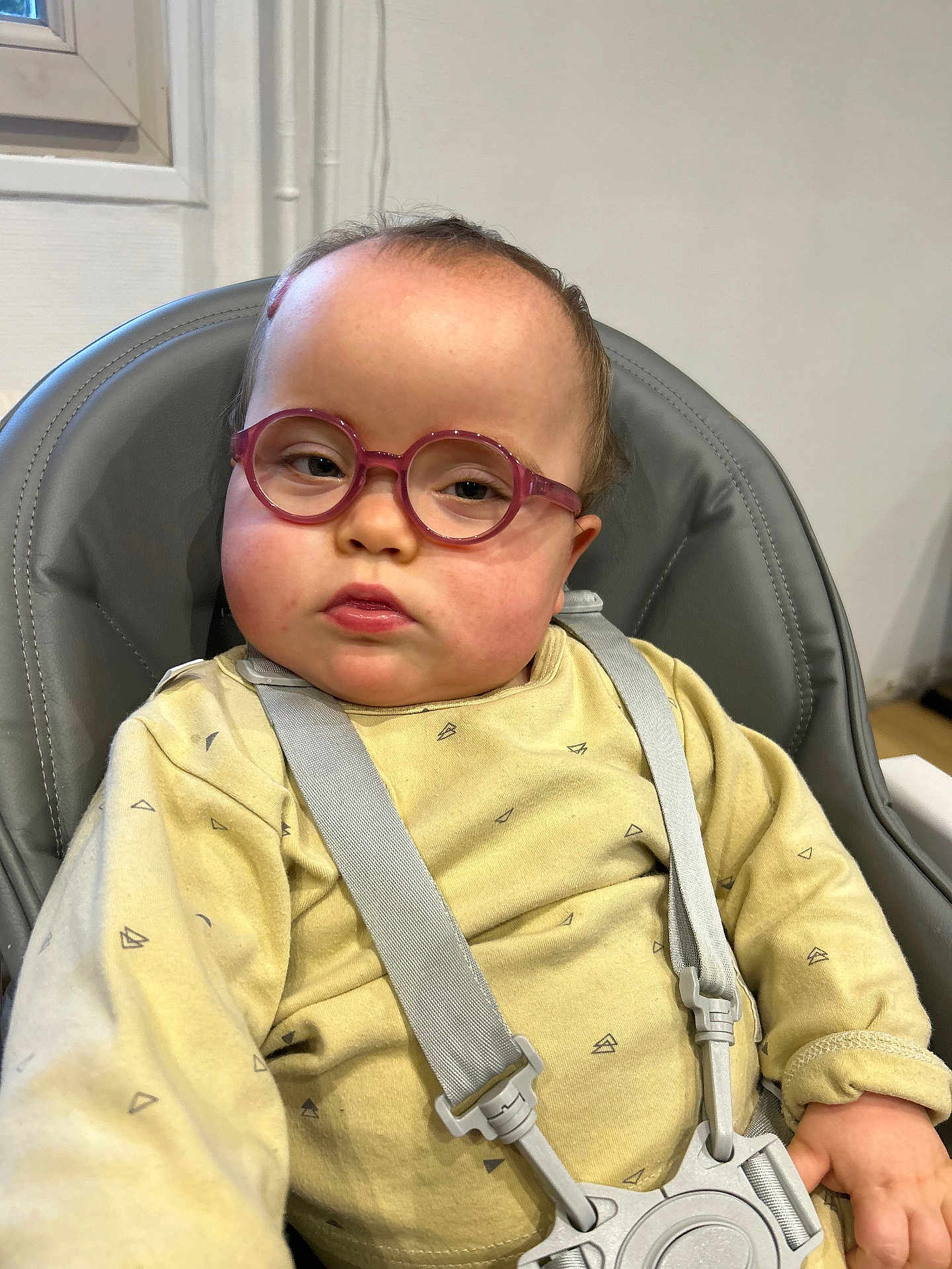 Zoe a rejoint le concours — aidez-le/la à gagner de superbes lots ! child, baby, toddler, glasses, pink_glasses, round_glasses, highchair, harness, seatbelt, yellow_clothing, chubby_cheeks, indoor, window, portrait, neutral_expression, skin, hair, photography, candid, furniture