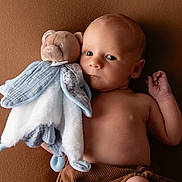 Léandre a rejoint le concours — aidez-le/la à gagner de superbes lots ! baby, infant, plush_toy, teddy_bear, soft_toy, brown_background, child, portrait, cute, bare_chest, newborn, comforter, lying_down, small_hand, warm_colors, indoor, peaceful, looking_away, fabric, cozy