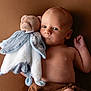 baby, infant, plush_toy, teddy_bear, soft_toy, brown_background, child, portrait, cute, bare_chest, newborn, comforter, lying_down, small_hand, warm_colors, indoor, peaceful, looking_away, fabric, cozy