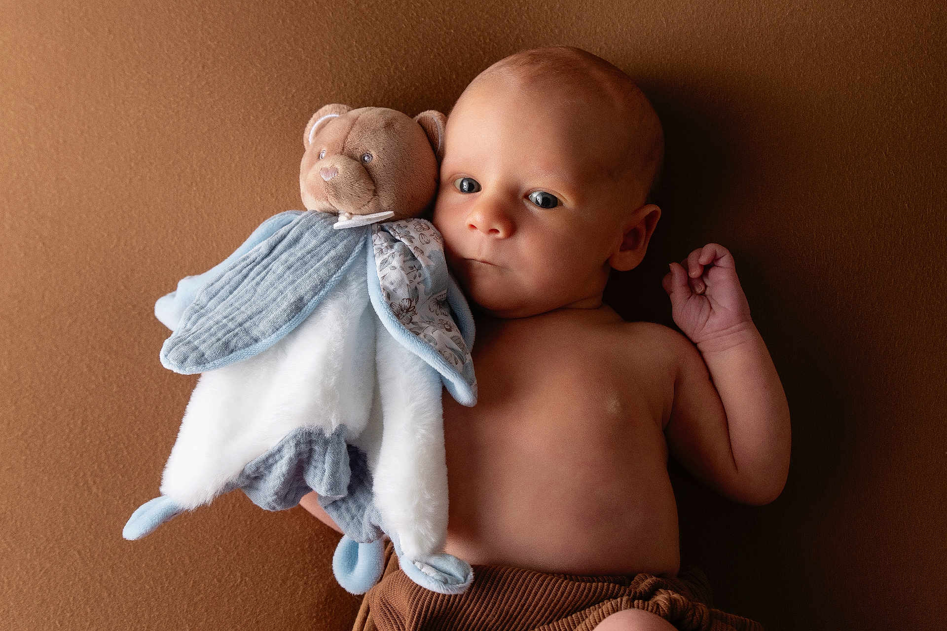 Léandre a rejoint le concours — aidez-le/la à gagner de superbes lots ! baby, infant, plush_toy, teddy_bear, soft_toy, brown_background, child, portrait, cute, bare_chest, newborn, comforter, lying_down, small_hand, warm_colors, indoor, peaceful, looking_away, fabric, cozy
