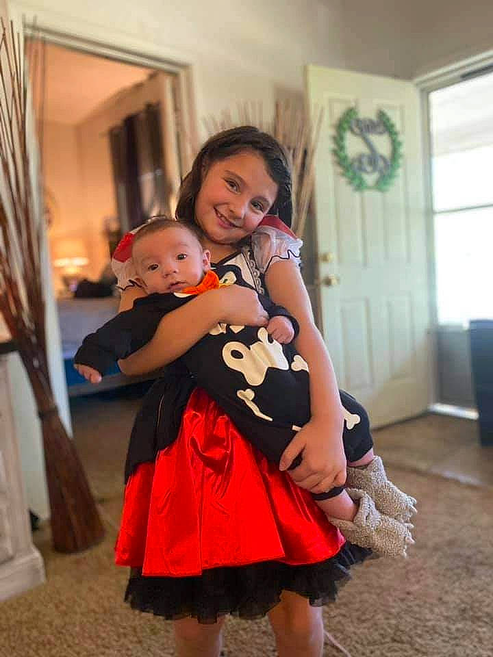 Ava is registered to the contest to win money with this photo: baby, costume, curtain, dress, event, eye, fashion_design, flooring, formal_wear, fun, happy, interaction, joy, necklace, one_piece_garment, party, person, sandal, shoulder, skin