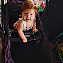 baby, babytrend, child, clothing, curious, face, grip, hand, head, indoor, patterned_dress, person, play_area, red_hair, seat, smiling, stroller, toddler, toys, white_dress