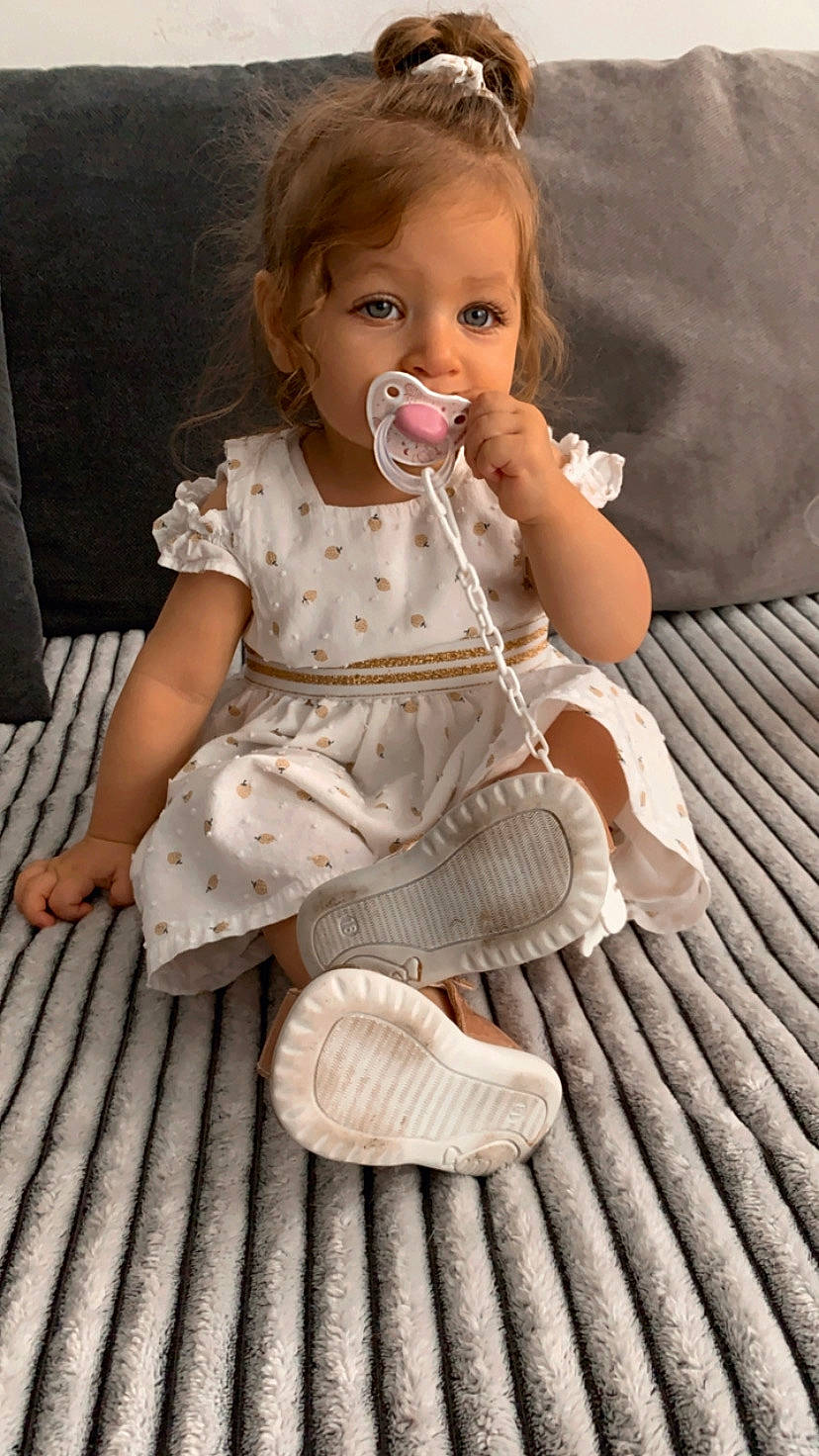 Analia participe au concours pour gagner de l'argent avec cette photo : arm, baby, baby_toddler_clothing, barefoot, cheek, child, clothing, dress, finger, flooring, foot, hand, happy, hardwood, human_leg, person, sitting, skin, sleeve, toddler