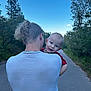 baby, child, clothing, daytime, earrings, forest, greenery, hair, happy, holding, nature, necklace, outdoor, path, person, road, shoulders, sky, smile, trees