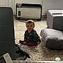 Jules participe au concours pour gagner de l'argent avec cette photo : carpet, child, clothing, cozy, curious, door, floor, flooring, furniture, heater, home, indoor, living_room, pajamas, person, remote_control, seated, toddler, toy, window