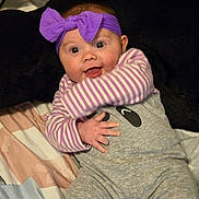 Gracelyn joined the competition — help win amazing prizes! baby, bed, blanket, candid, child, cute, expressive, gray_clothing, happy, headband, indoors, infant, onesie, person, portrait, purple_bow, smiling, soft_toys, striped_shirt, young