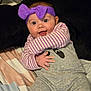 baby, bed, blanket, candid, child, cute, expressive, gray_clothing, happy, headband, indoors, infant, onesie, person, portrait, purple_bow, smiling, soft_toys, striped_shirt, young