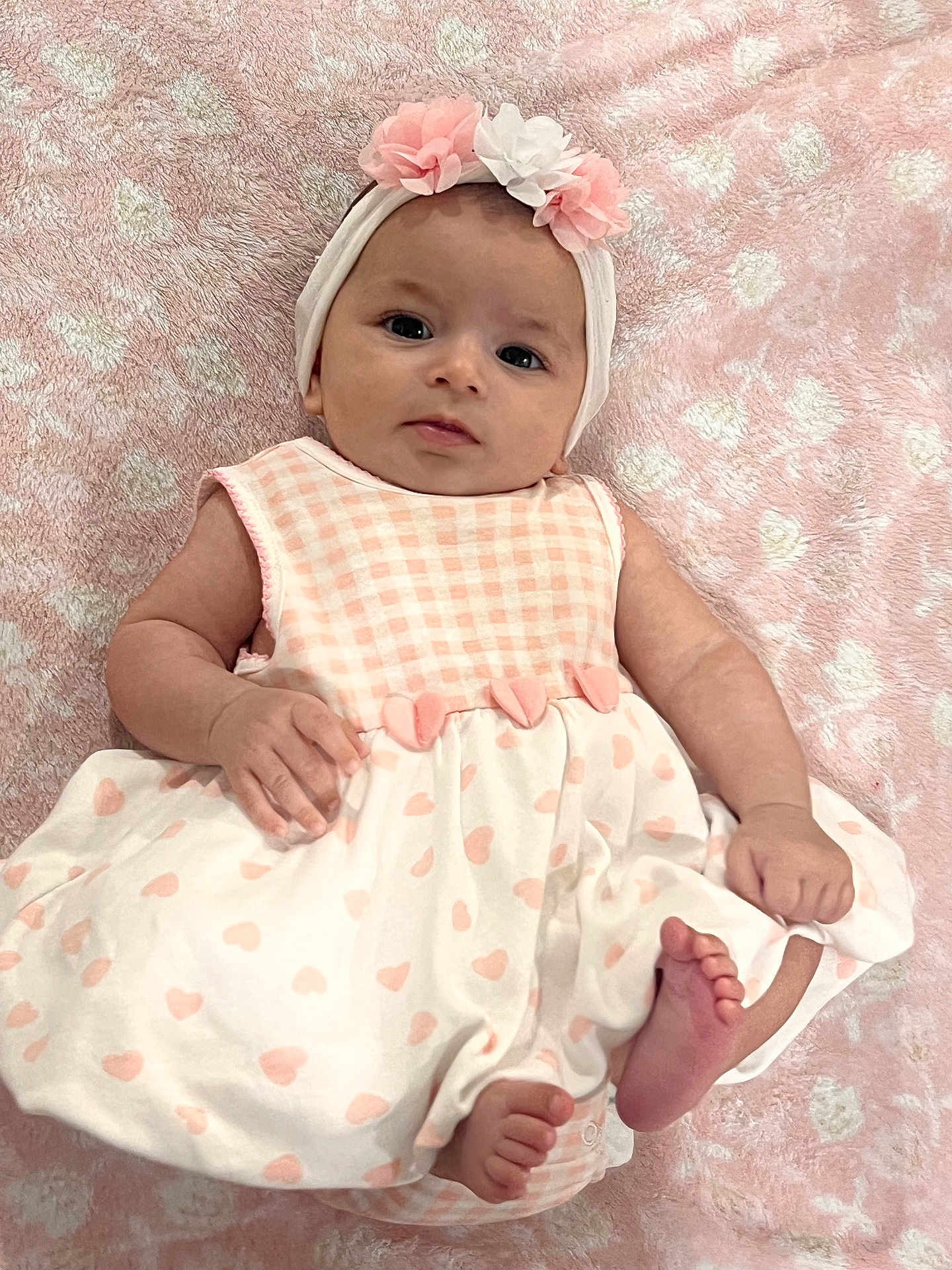 Aria is registered to the contest to win money with this photo: baby, infant, child, dress, headband, flower, pink, white, heart_pattern, blanket, soft_texture, cute, lying_down, feet, hand, face, portrait, adorable, skin, person