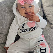 Nina a rejoint le concours — aidez-le/la à gagner de superbes lots ! baby, child, smiling, hoodie, pink_bow, white_clothing, pants, sitting, couch, indoor, happy, cute, infant, face, person, playful, cozy, casual_wear, portrait, toddler