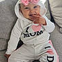 baby, child, smiling, hoodie, pink_bow, white_clothing, pants, sitting, couch, indoor, happy, cute, infant, face, person, playful, cozy, casual_wear, portrait, toddler
