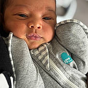 Kylo is registered to the contest to win money with this photo: baby, infant, face, close_up, grey_clothing, sleepy, cute, soft_skin, newborn, zipped_jacket, striped_pattern, blue_heart_patch, cozy, warm, portrait, human, child, young, indoors, expression