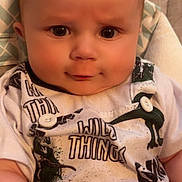 Archer is registered to the contest to win money with this photo: baby, child, infant, face, eyes, clothing, dinosaur_print, smile, sitting, cute, young_child, person, portrait, indoors, white_shirt, button, fabric, seatbelt, closeup, head