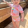toddler, child, smiling, outdoor, sunlight, pink_clothing, ice_cream_graphic, shorts, shirt, barefoot, standing, wooden_fence, happy, person, skin, face, arm, daylight, cute, young
