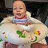 baby, bright_eyes, child, colorful, dinosaur_pattern, face, feet, happy, home, indoor, infant, inflatable_ring, kitchen, moon, person, playful, smiling, stars, striped_shirt, toy