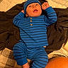 baby, blanket, blue_clothing, child, cozy, curious_expression, cute, foot, hat, indoor, infant, lying_down, person, portrait, raised_fists, relaxing, soft_texture, striped_outfit, warm_lighting, young_baby