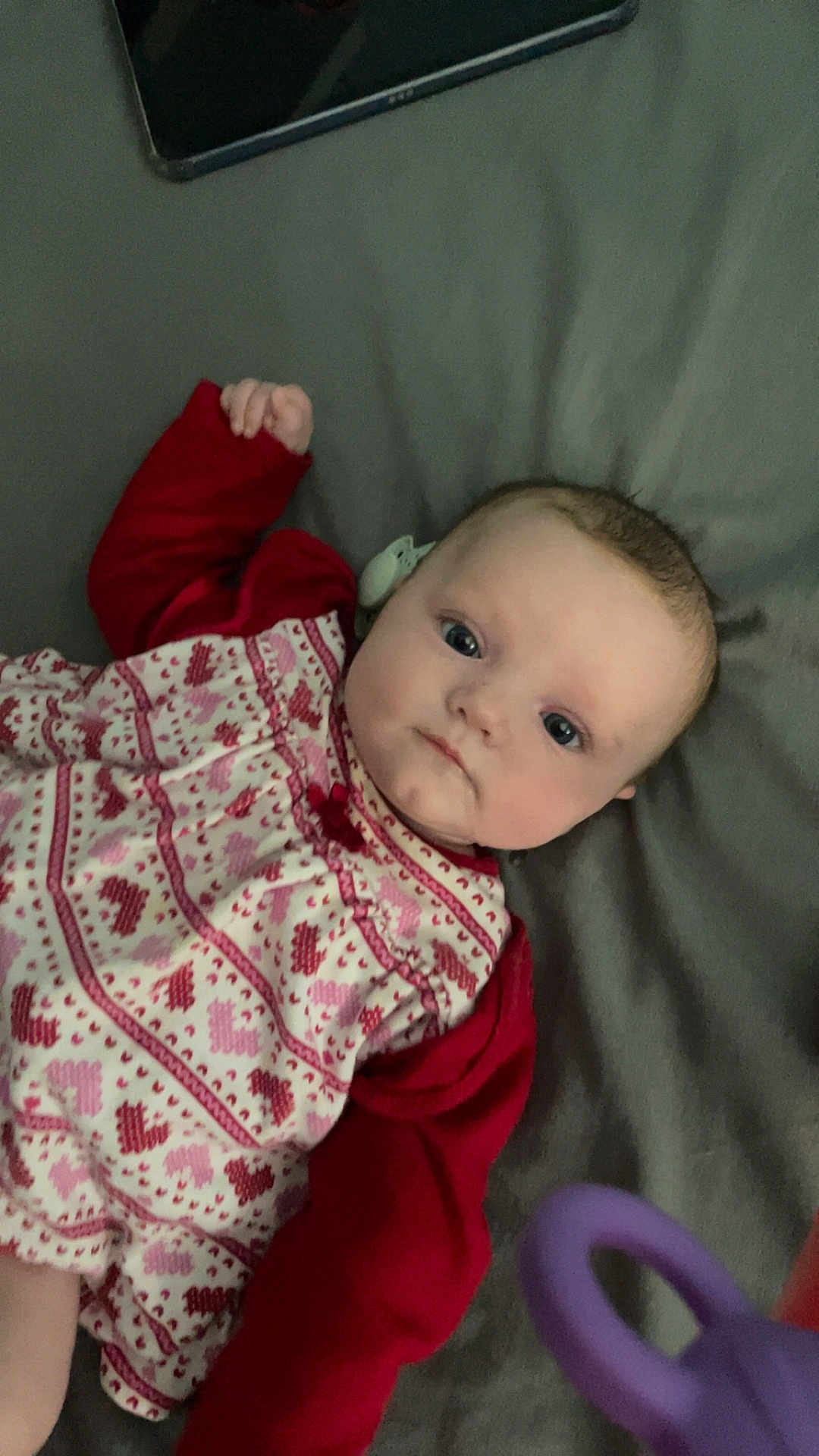 Lottie-May joined the competition — help win amazing prizes! baby, infant, child, face, eyes, clothing, red_sleeves, patterned_dress, lying_down, blanket, toy, purple_toy, indoor, portrait, cute, young, skin, head, hand, expression