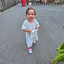 Nora a rejoint le concours — aidez-le/la à gagner de superbes lots ! child, girl, white_dress, purse, shoes, outdoor, palm_tree, paved_road, people, plant, umbrella, fence, building, greenery, smiling, walking, daylight, vacation, casual, happy