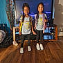 child, children, girls, siblings, matching_outfits, backpacks, smiling, indoor, living_room, television, wood_floor, casual_clothing, braided_hair, shoes, home, furniture, happy, person, portrait, together