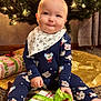 baby, infant, child, christmas_tree, ornament, string_lights, present, gift, wrapping_paper, green_ribbon, bib, onesie, smile, sitting, carpet, holiday, festive, indoor, tree_skirt, cute