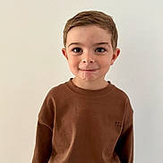 Sandro participe au concours pour gagner de l'argent avec cette photo : child, boy, smile, brown_sweater, blue_jeans, casual, indoor, portrait, sitting, short_hair, playful, face, person, cute, young, mischievous, light_background, happy, fashion, clothing