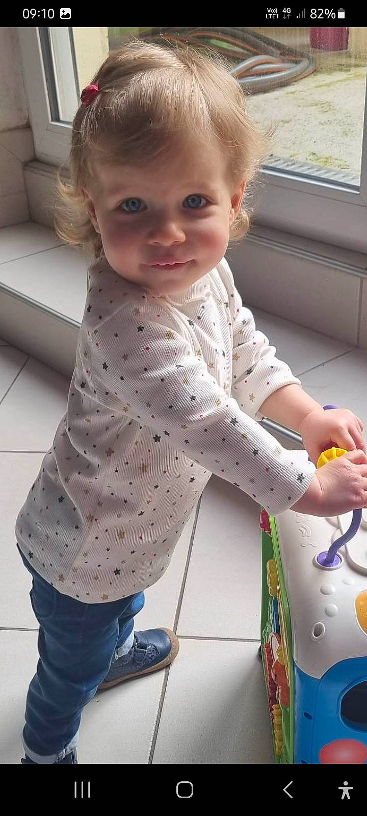 Lola a rejoint le concours — aidez-le/la à gagner de superbes lots ! baby, baby_products, baby_toddler_clothing, child, clothing, face, finger, flooring, gesture, hand, pattern, person, play, sitting, sleeve, snapshot, standing, t_shirt, textile, thumb