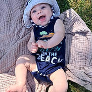 Hollis is registered to the contest to win money with this photo: baby, infant, child, smiling, happy, outdoor, grass, blanket, quilt, sun_hat, romper, summer, portrait, lying_down, looking_at_camera, blue_eyes, sunlight, garden, playful, photography