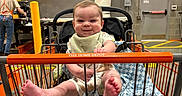 Hollis joined the competition — help win amazing prizes! baby, child, shopping_cart, hardware_store, home_depot, indoors, smiling, sitting, blanket, bib, infant, portrait, retail, lumber, wood, cart, orange, exit_sign, store, happy