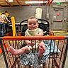 baby, child, shopping_cart, hardware_store, home_depot, indoors, smiling, sitting, blanket, bib, infant, portrait, retail, lumber, wood, cart, orange, exit_sign, store, happy