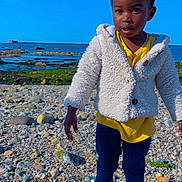 Floriane participe au concours pour gagner de l'argent avec cette photo : beach, blue_sky, casual_clothing, child, cute, daylight, hair_ties, jacket, nature, navy_pants, ocean, outdoor, pink_sandals, portrait, rocks, standing, summer, toddler, water, yellow_shirt