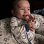 baby, child, clapping, comfort, cozy, cushion, cute, hand_gesture, happy, indoor, infant, leaf_pattern, onesie, person, portrait, seated, smiling, soft_lighting, sports_pattern, young