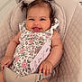 baby, smiling, infant, floral_clothing, baby_seat, plush_toy, card, indoor, cute, happy, person, child, hair_ties, pigtails, seatbelt, soft_toys, home, portrait, sitting, nursery