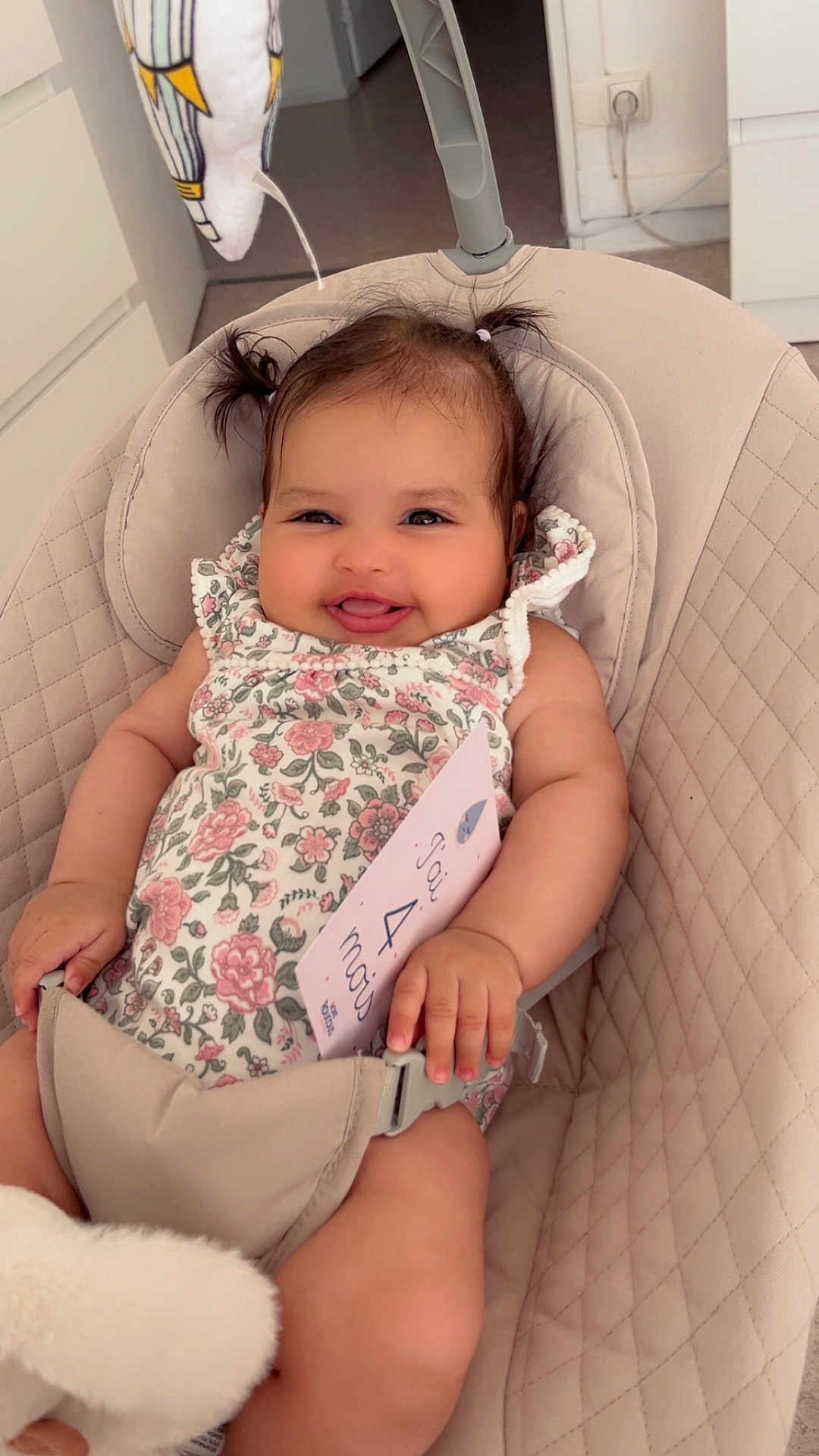 Malak participe au concours pour gagner de l'argent avec cette photo : baby, smiling, infant, floral_clothing, baby_seat, plush_toy, card, indoor, cute, happy, person, child, hair_ties, pigtails, seatbelt, soft_toys, home, portrait, sitting, nursery