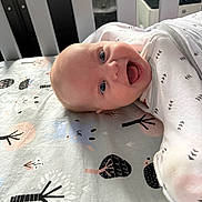 Leila is registered to the contest to win money with this photo: baby, smiling, crib, bedding, pattern, animal_print, tree_print, infant, happy, cute, child, face, blue_eyes, white_clothing, laying_down, indoors, soft_lighting, closeup, head, portrait