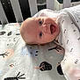 baby, smiling, crib, bedding, pattern, animal_print, tree_print, infant, happy, cute, child, face, blue_eyes, white_clothing, laying_down, indoors, soft_lighting, closeup, head, portrait
