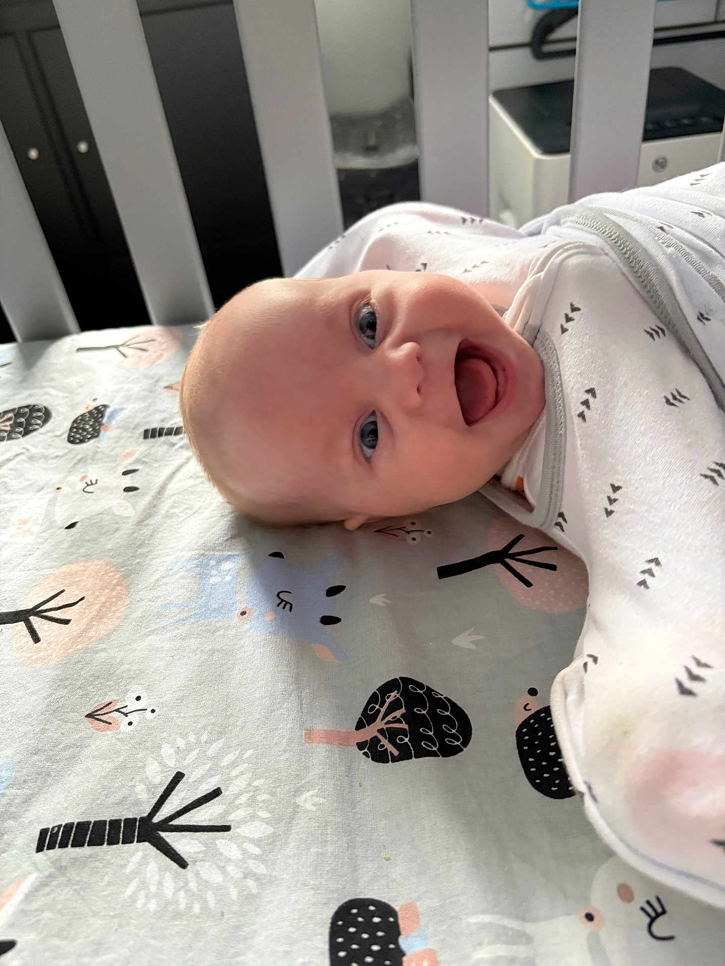 Leila is registered to the contest to win money with this photo: baby, smiling, crib, bedding, pattern, animal_print, tree_print, infant, happy, cute, child, face, blue_eyes, white_clothing, laying_down, indoors, soft_lighting, closeup, head, portrait