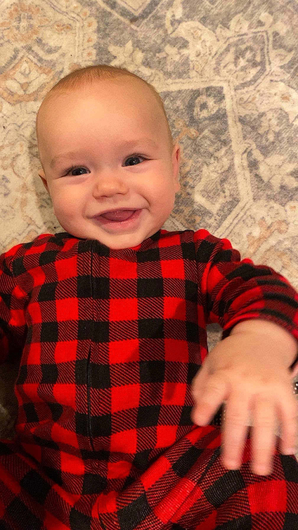 Jasper joined the competition — help win amazing prizes! baby, infant, child, smile, smiling, portrait, cute, lying_down, red_plaid, onesie, sleepwear, carpet, floor, home, cheerful, hand, eyes, head, skin, happy