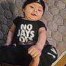Ivan is registered to the contest to win money with this photo: baby, child, infant, smiling, hat, clothing, black_outfit, text_on_clothing, lying_down, carpet, mat, foot, hand, face, cute, indoors, playful, happy, person, portrait