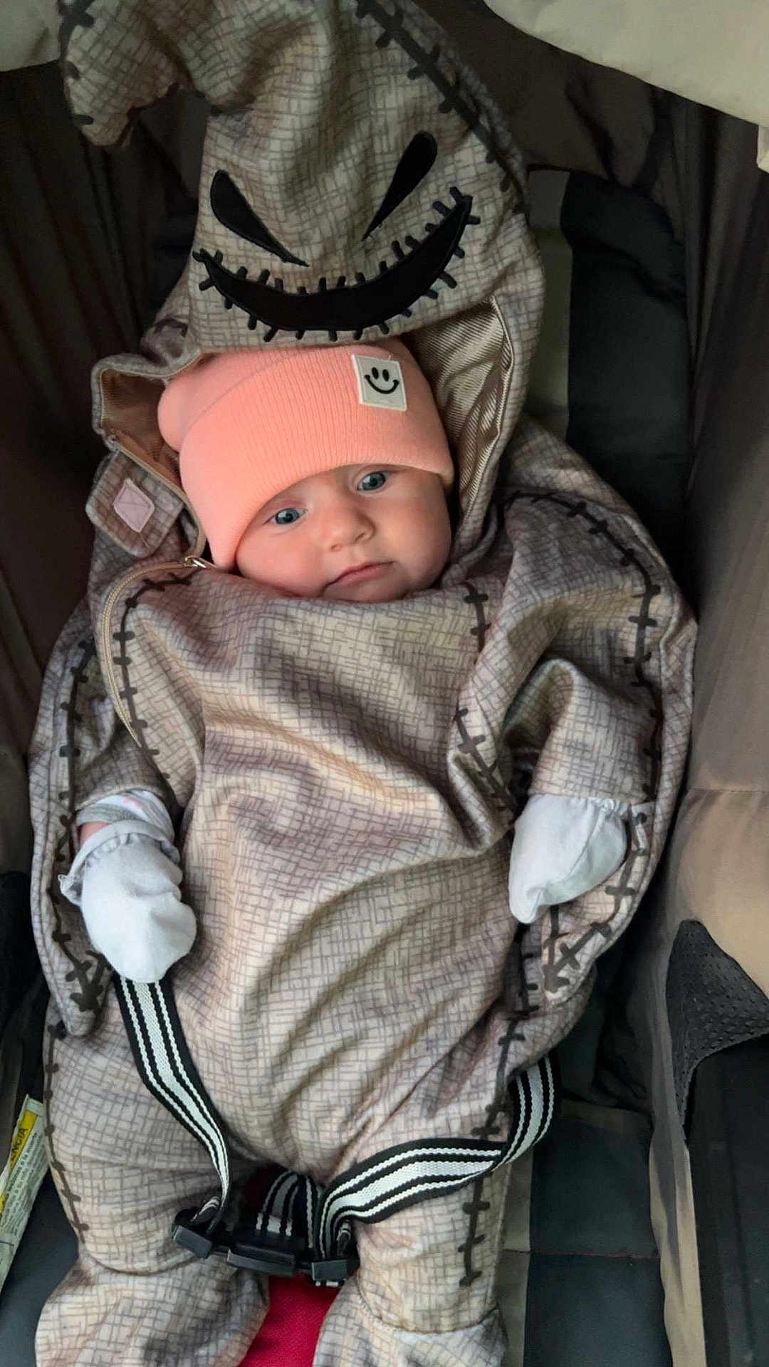 Autumn is registered to the contest to win money with this photo: baby, infant, car_seat, onesie, hood, pink_beanie, smiley_patch, patterned_clothing, face, straps, mittens, cute, cozy, child, seatbelt, indoor, portrait, expression, warm_clothing, babywearing