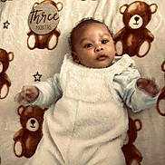 Louis is registered to the contest to win money with this photo: baby, infant, teddy_bear, blanket, plush, pattern, wooden_plaque, three_months, clothing, white_outfit, cute, lying_down, child, portrait, soft, cozy, star_pattern, newborn, face, hands