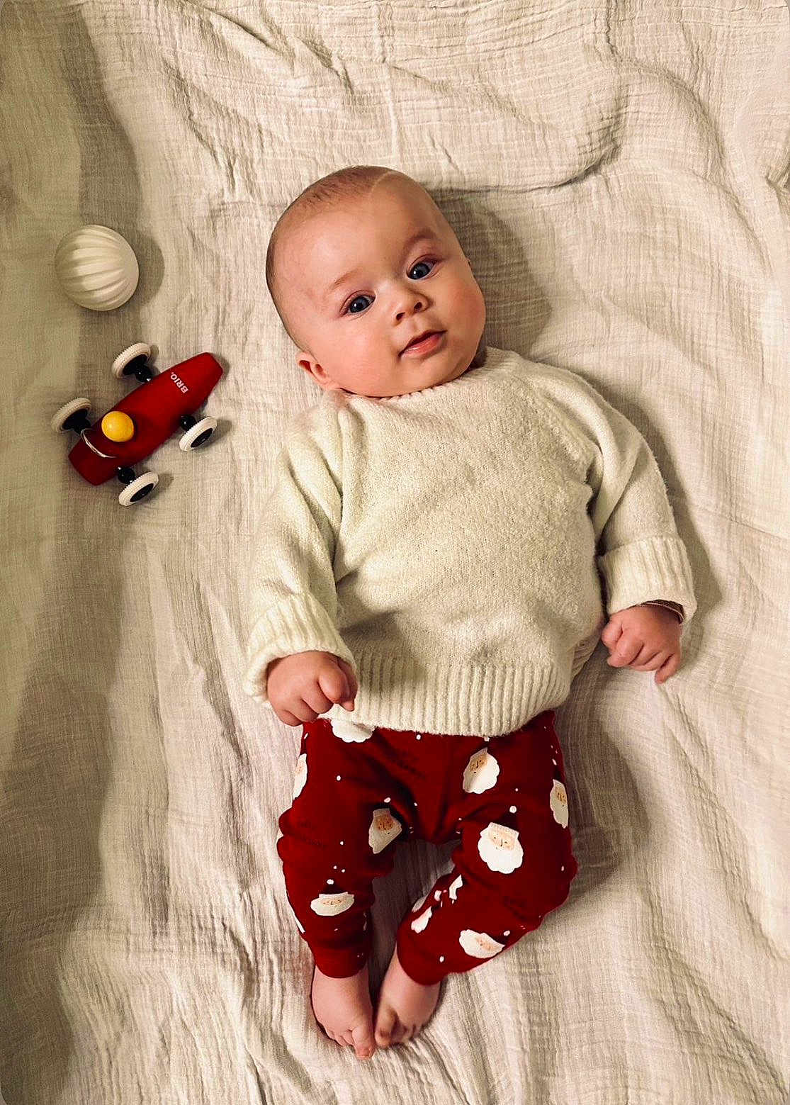 Ezio a rejoint le concours — aidez-le/la à gagner de superbes lots ! baby, infant, blanket, toy_car, white_ball, red_pants, santa_print, sweater, lying_down, cute, child, face, fingers, feet, indoors, soft_texture, expression, looking_at_camera, playtime, holiday_theme