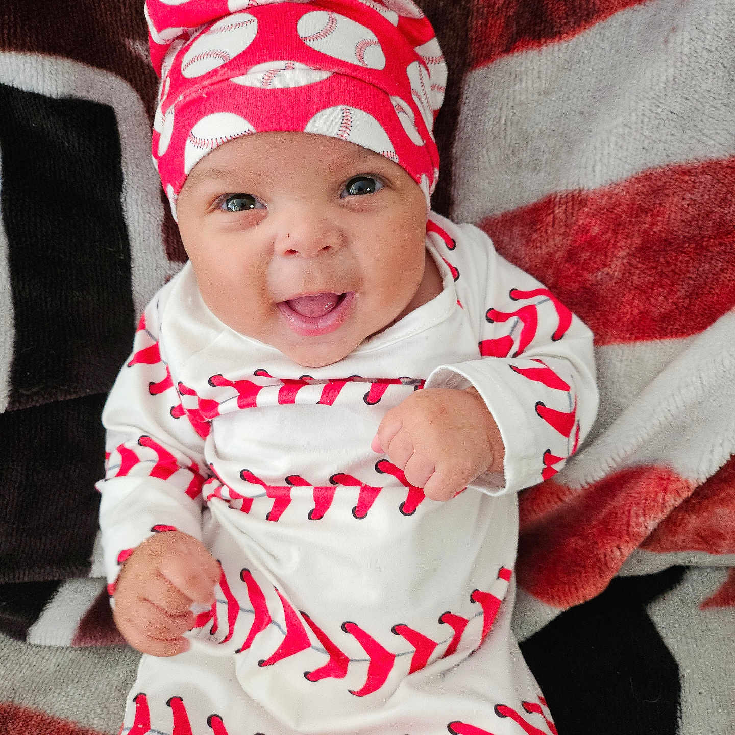 Deantre is registered to the contest to win money with this photo: apparel, baby, baseball_pattern, blanket, cheerful, child, clothing, cozy, cute, fist, happy, hat, headwear, indoors, infant, lying_down, patterned_blanket, portrait, smiling, young_child