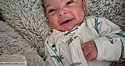 Deantre is registered to the contest to win money with this photo: baby, blanket, child, clothing, cozy, cute, dinosaur_onesie, face, fuzzy_blanket, gray_blanket, happy, indoor, infant, lying_down, newborn, person, pink_blanket, portrait, smiling, soft_texture