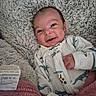 baby, blanket, child, clothing, cozy, cute, dinosaur_onesie, face, fuzzy_blanket, gray_blanket, happy, indoor, infant, lying_down, newborn, person, pink_blanket, portrait, smiling, soft_texture