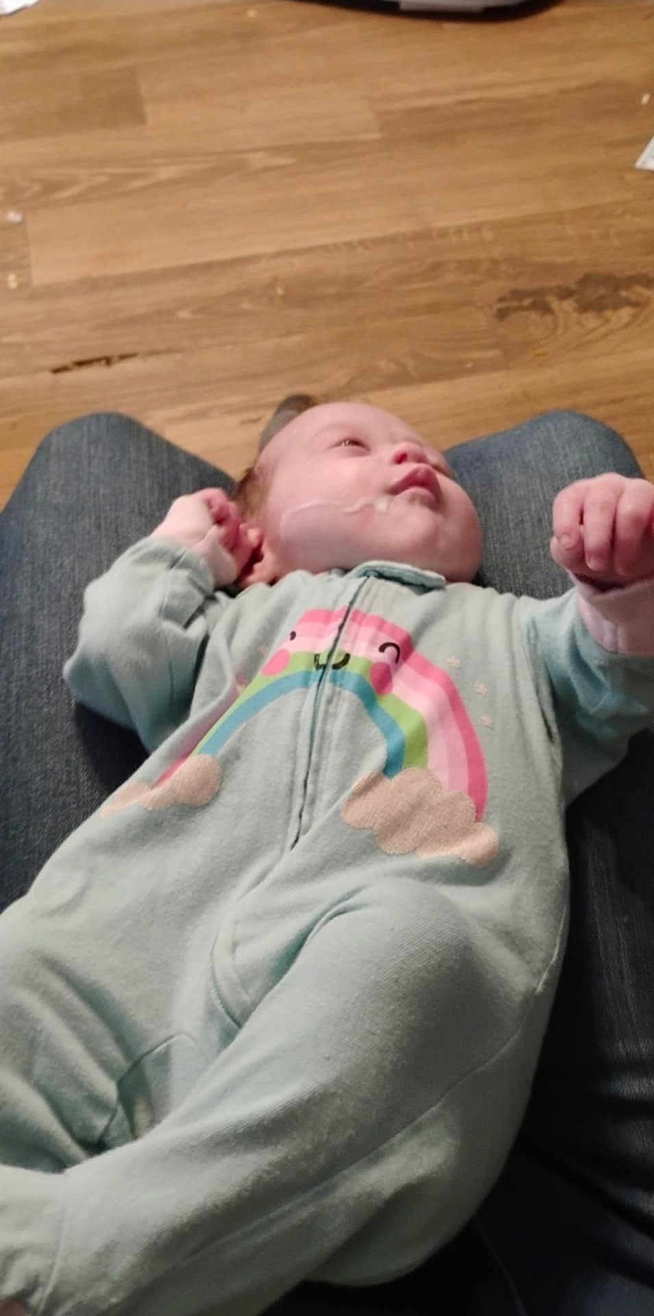 Pam joined the competition — help win amazing prizes! baby, infant, onesie, rainbow, person, clothing, floor, wooden_floor, lap, resting, casual, indoor, cute, child, soft_colors, young, sleepy, hand, face, cozy